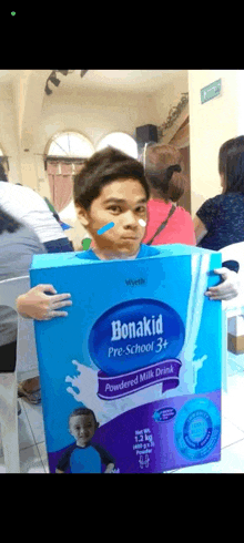 a boy is holding a box of bonakid pre school powdered milk drink .