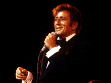 a man in a tuxedo is singing into a microphone on stage