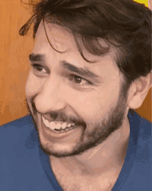 a man with a beard and a blue shirt is smiling and making a funny face .