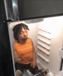 a man is sitting in an open refrigerator eating a sandwich .