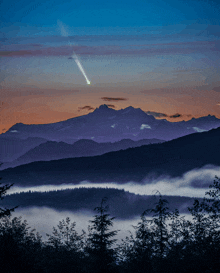 a shooting star is visible in the night sky over a mountain range