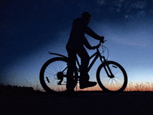 a silhouette of a person riding a bike with a blue sky behind them