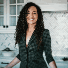 a woman with curly hair wearing a plaid jacket is smiling