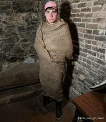 a man wrapped in a burlap blanket stands in front of a stone wall