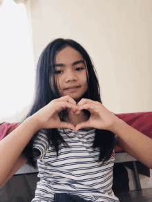 a young girl in a striped shirt makes a heart shape with her hands