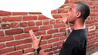 a man standing in front of a brick wall with a white speech bubble above his head