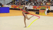 a female gymnast is performing with a colorful ribbon in front of a crowd with a sign that says tdp