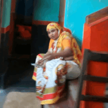 a woman in a colorful outfit sits on a stool in front of a blue wall