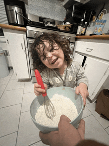 a little girl is holding a bowl of flour and a red whisk