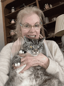 a woman with glasses is holding a cat with a yellow eye