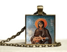 a square pendant with a picture of a woman holding a cross on a chain on a table .