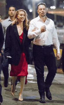 a man in a white shirt and a woman in a red dress walk down the street