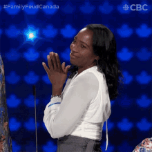 a woman applauds while standing in front of a microphone with a blue background and the words family feud canada on the bottom