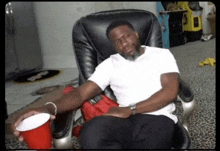 a man is sitting in a chair with a red cup in his hand