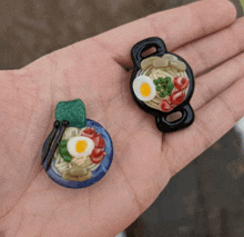 a hand holding a bowl of noodles and a pot of noodles with eggs