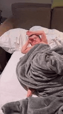 a young boy is sleeping on a bed with a blanket covering him .