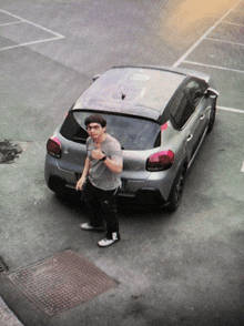 a man is standing in front of a silver car that says citroen on the back