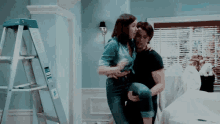 a man is carrying a woman in his arms in a room with a ladder in the background .