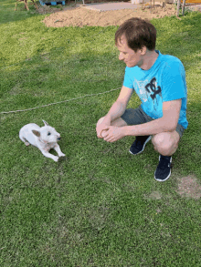 a man in a blue shirt with the letter d on it is kneeling down next to a white dog