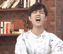 a young man is making a funny face while sitting in front of a bookshelf with books on it .