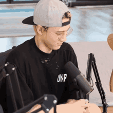 a man wearing a hat and glasses sitting in front of a microphone