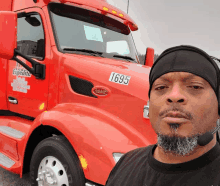 a man taking a selfie in front of a red truck with the number 1695 on the front