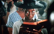 a woman wearing glasses and a hat holds a book