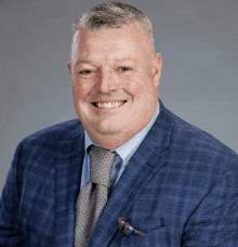 a man in a blue suit and tie is smiling for the camera