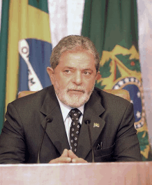 a man in a suit and tie is sitting at a podium in front of a flag