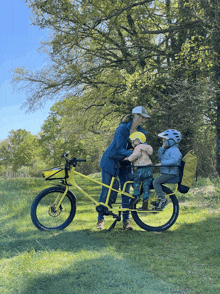 a woman rides a yellow bicycle with two children on it