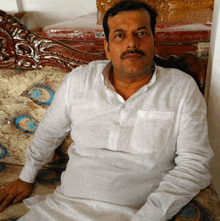 a man in a white shirt sits on a couch with a peacock cushion