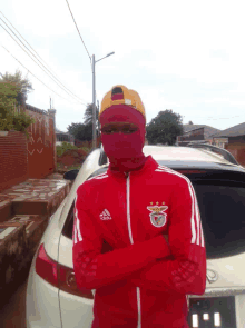 a man wearing a red adidas jacket is standing in front of a car