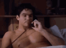 a shirtless man is talking on a phone while laying in bed .