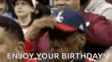 a group of people are sitting in a stadium and one of them is wearing a red white and blue baseball cap .