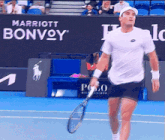 a man holding a tennis racquet on a tennis court with a marriott bonvoy banner behind him