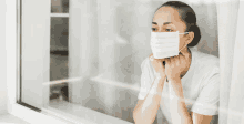 a woman wearing a face mask is looking out a window