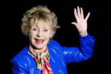 a woman in a blue jacket and scarf is waving at the camera .