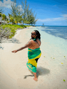 a woman in a green yellow and black sarong is standing on a beach