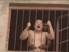 a man without a shirt is behind bars in a window .