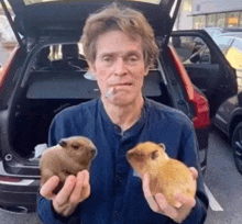 a man smoking a cigarette while holding two small animals in front of a car .