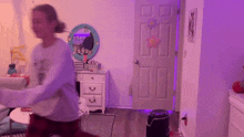 a girl is dancing in a bedroom with purple lights on the wall .