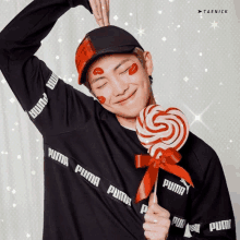 a man wearing a black puma shirt is holding a red lollipop