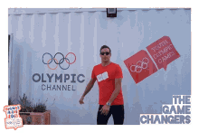 a man stands in front of an olympic channel advertisement