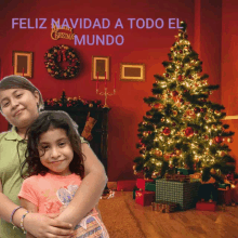 two little girls are hugging in front of a christmas tree with feliz navidad a todo el mundo written on it