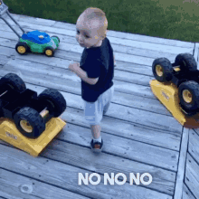 a baby is standing on a wooden deck next to toy trucks and a sign that says no on no