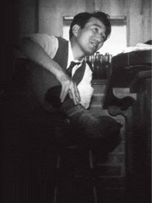 a man in a vest and tie sits on a stool