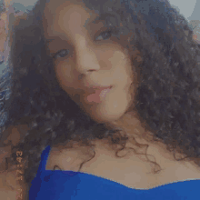 a young woman with curly hair is taking a selfie in a blue top .