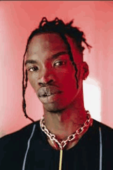 a young man with dreadlocks and a chain around his neck is wearing a black shirt .