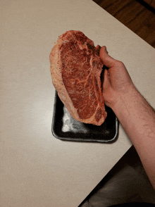 a person is holding a large piece of meat over a styrofoam tray