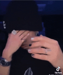 a person is covering their face with their hands while wearing a black hat .